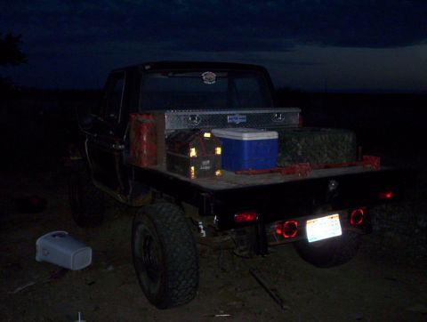 1978 Ford Bronco - A black Ford pickup truck with a flatbed is parked at night, loaded with various items.