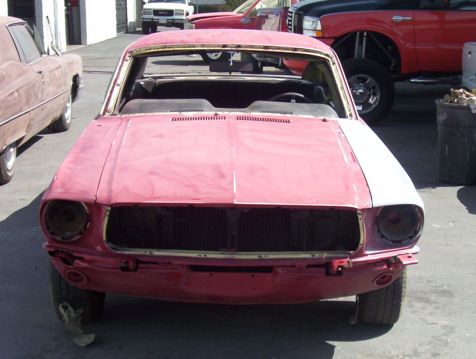 Faded red Mustang fastback project car in primer parked in a shop yard