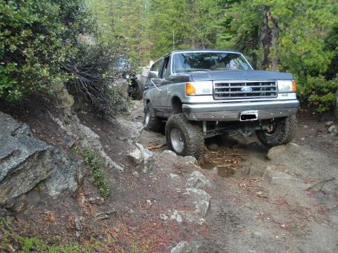 1989 Ford Bronco - This lifted 1989 Ford Bronco tackles a challenging rocky path, with another vehicle visible in the background.