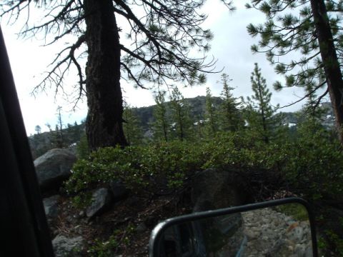 1989 Ford Bronco - View from inside a vehicle shows a rocky, wooded landscape with a side mirror reflecting the trail ahead.
