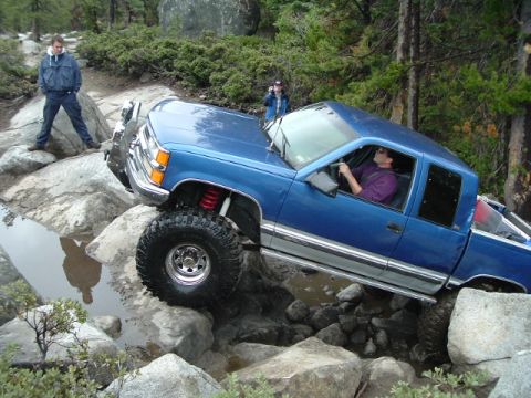 1989 Ford Bronco - Pickup truck tackling a difficult off-road course with large rocks and water.