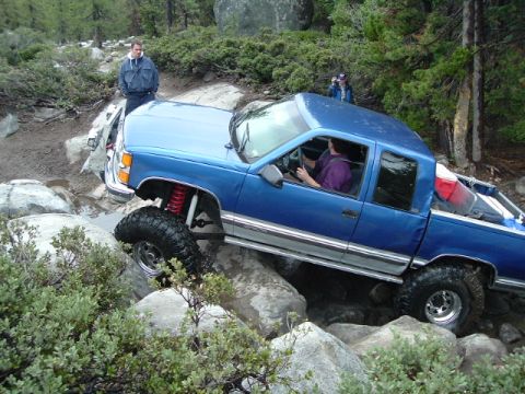 1989 Ford Bronco - A blue pickup truck is shown navigating a rocky trail, with two people observing the action.