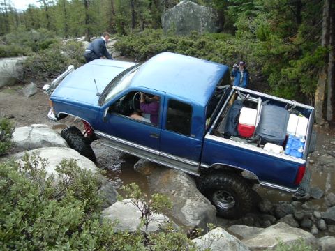 1989 Ford Bronco - A blue pickup truck is shown navigating a challenging rocky terrain on an off-road trail.