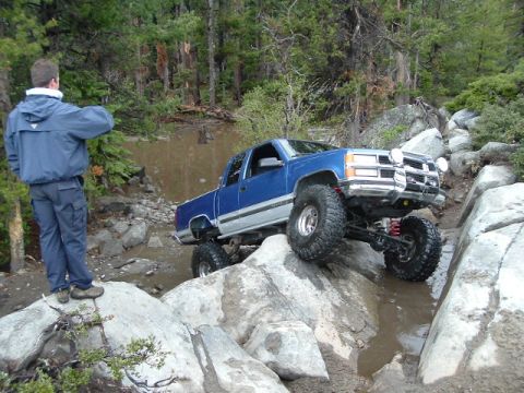 1989 Ford Bronco - A lifted pickup truck tackles a challenging off-road obstacle course with a person observing the action.