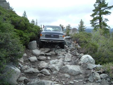 1989 Ford Bronco - A Ford Bronco drives over a boulder-strewn path on a cloudy day.