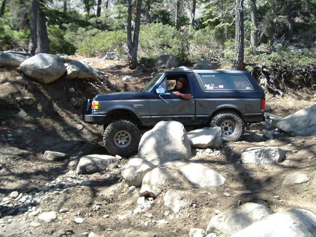 Dark blue Ford Bronco crawling over granite boulders on a forest rock trail