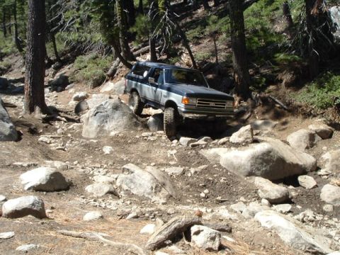 1989 Ford Bronco - Ford Bronco tackling a difficult off-road path with large rocks and trees.