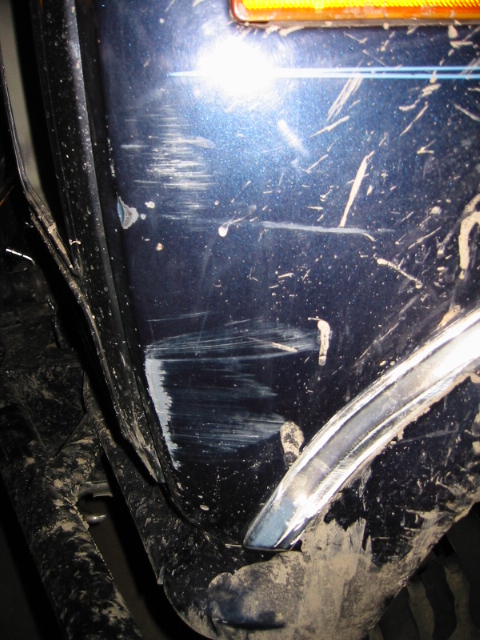1985 Ford Bronco - Close-up of a damaged blue fender on a vehicle, showing significant scratches and scuff marks.