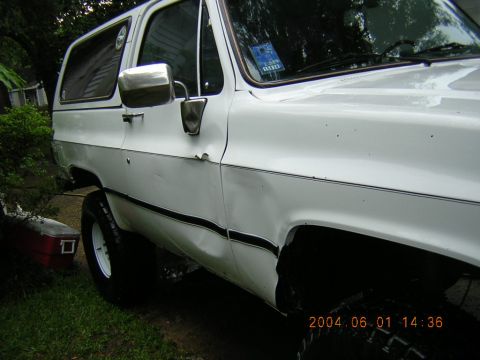 1984 Chevrolet Blazer - The vehicle has a dent on the rear passenger side panel and a red toolbox is visible on the grass.