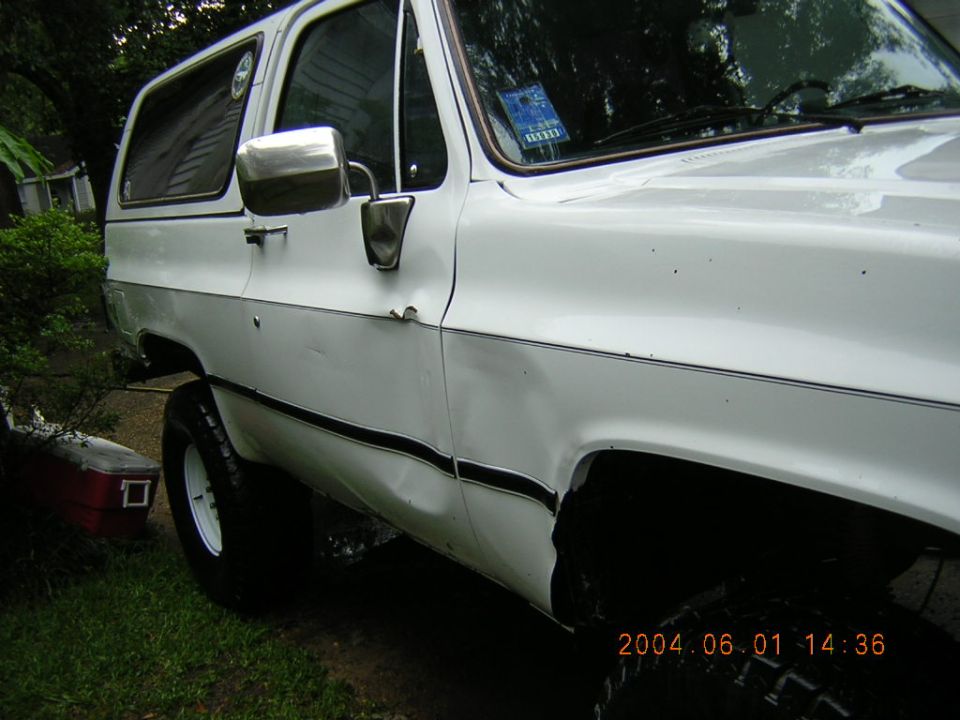 White SUV, side view. Has a dent on the rear quarter panel and a red toolbox on the ground