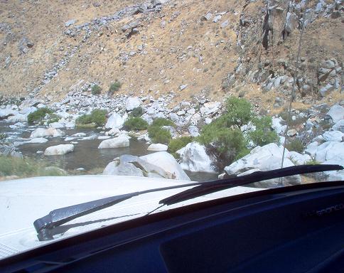 Interior view of a vehicle driving past a rocky river and dry hillside