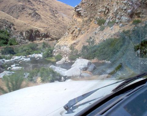 1988 Ford Bronco - Driving through a scenic mountain pass with a river flowing alongside the road.