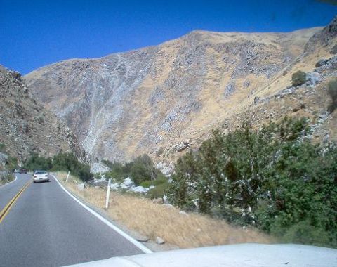 1988 Ford Bronco - A road winds through a canyon with dry hillsides and sparse vegetation, with two cars visible on the asphalt.
