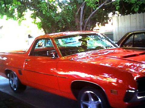 1970 Ford Ranchero - The side profile of a bright red 1970 Ford Ranchero GT is visible, parked outdoors.