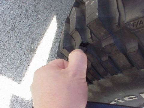 1989 Ford Bronco - Close-up of a tire tread, with a hand pointing to a section of the sidewall.