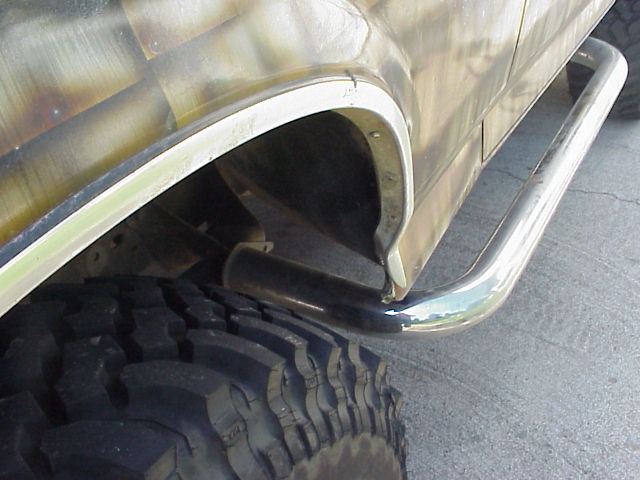Side view of a vehicle's rear wheel well with large tire and chrome side step