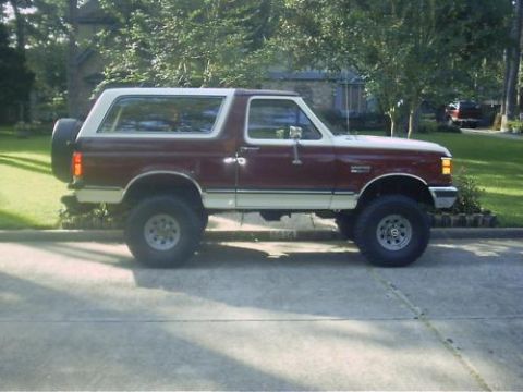 1990 Ford Bronco - Side profile of a lifted two-tone burgundy-over-tan full-size Ford Bronco with a covered rear-mounted spare tire, alloy wheels with oversiz…