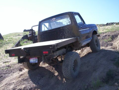 1978 Ford Bronco - This Ford truck, likely from the late 1970s, navigates a dirt trail with a flatbed in the rear.