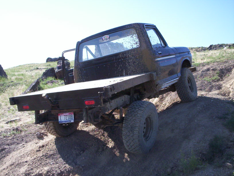 Ford flatbed truck driving off-road, mud splattered on body. License plate E 72188