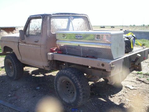 1978 Ford Bronco - This flatbed truck, likely from the 1970s, is heavily coated in mud and has a large toolbox mounted in its bed.