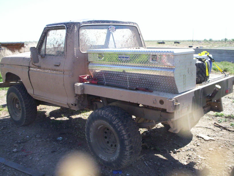 Mud-covered flatbed truck with a diamond plate toolbox and spare tire in the bed