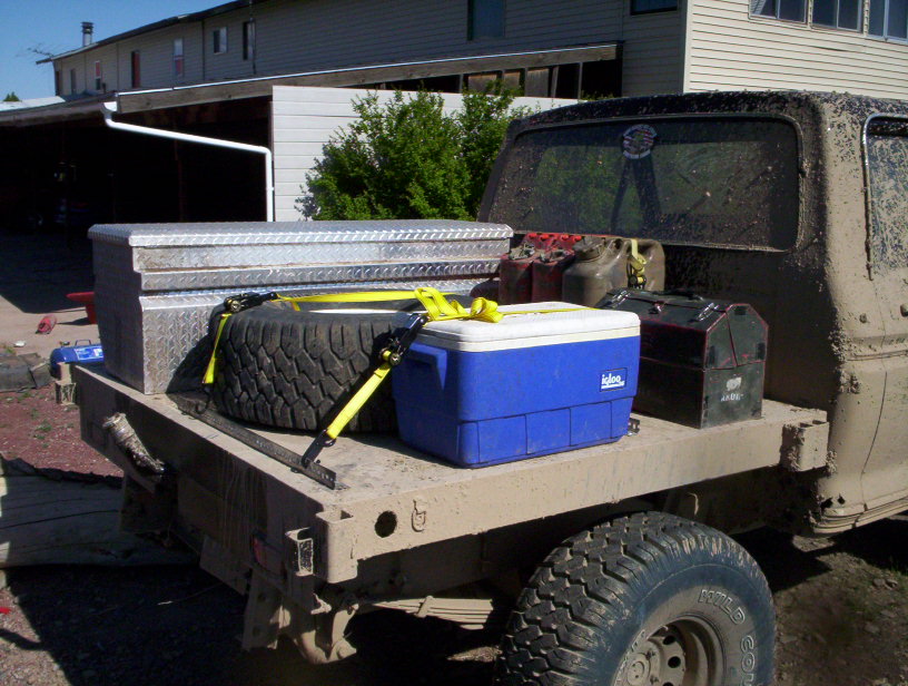 Flatbed truck bed loaded with a toolbox, spare tire, cooler, and gas cans