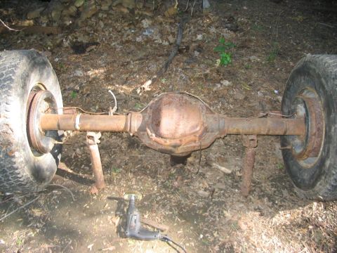 1986 Ford Bronco - A heavily rusted rear axle assembly, likely from an older truck or SUV, sits outdoors with tires attached.