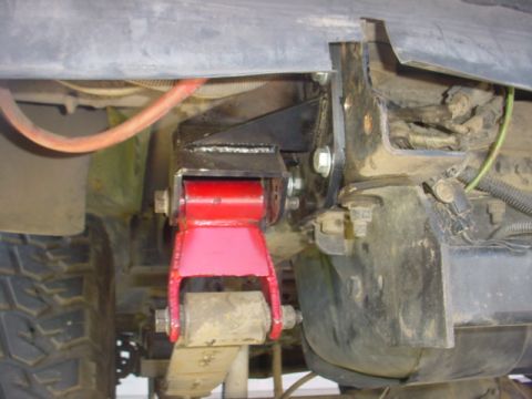 1988 Ford Bronco - Close-up view of a red shackle flip bracket modification on a vehicle's suspension system.