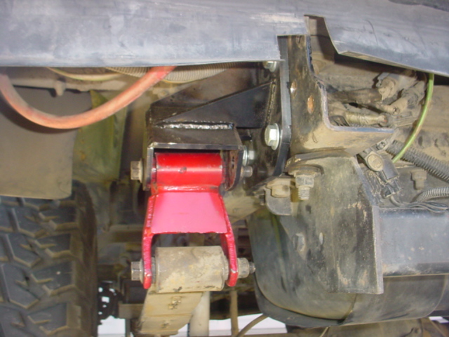 Red leaf spring shackle and frame hanger under a truck with mud-terrain tire