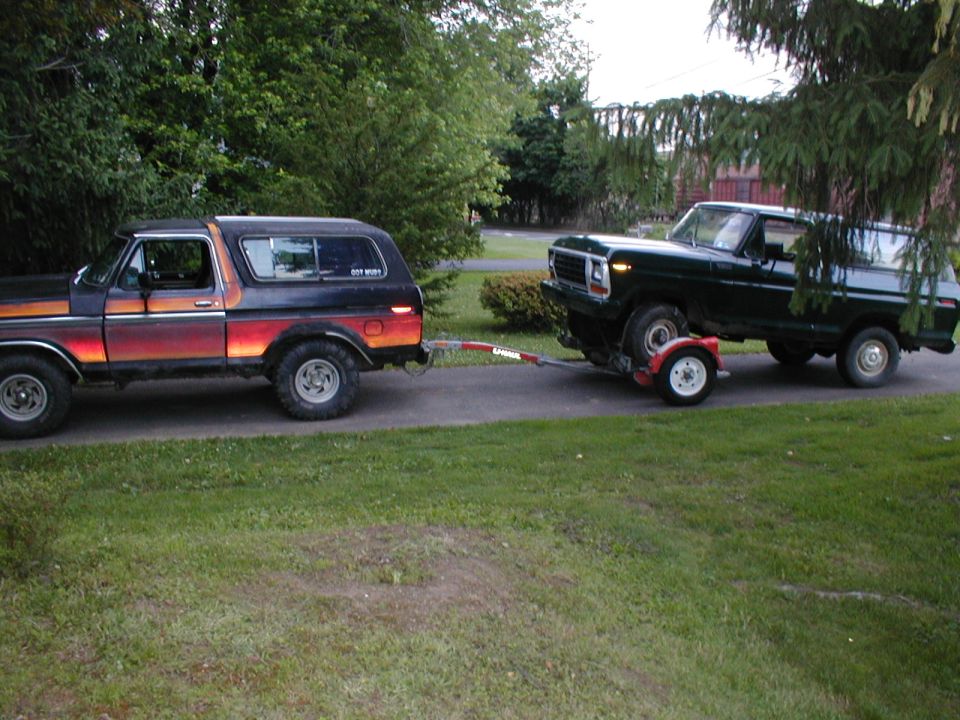 1978 Ford Bronco towing a 1979 Ford Bronco on a trailer. Both vehicles are dark colored