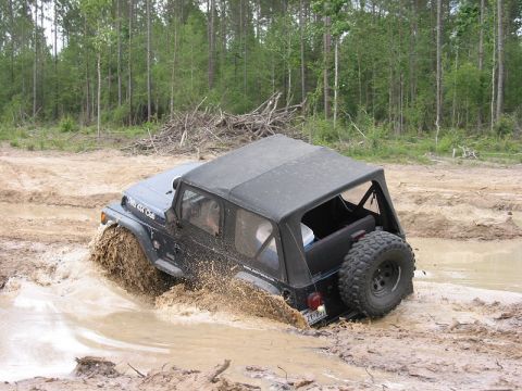 2002 Jeep Wrangler - A Jeep Wrangler navigates a muddy trail, kicking up water and dirt.