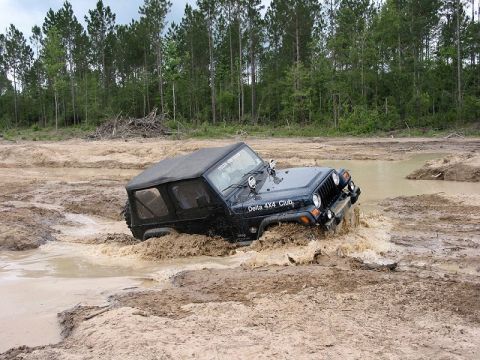 2002 Jeep Wrangler - A black Jeep Wrangler navigates through a muddy off-road course, with water splashing around its front.