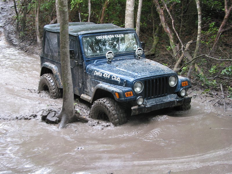 Blue Jeep Wrangler TJ with Delta 4X4 Club decals fording a muddy trail water crossing