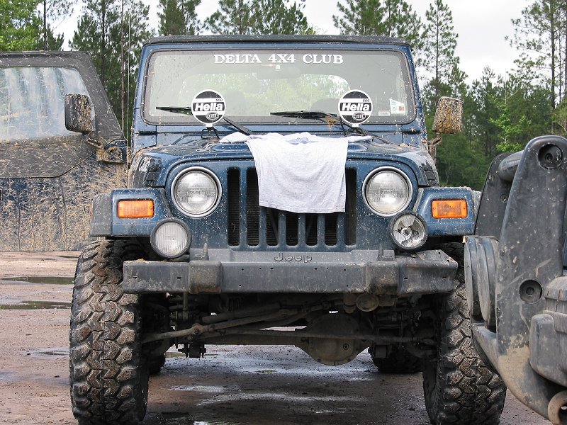Front view of muddy lifted blue Jeep Wrangler with Delta 4x4 Club banner