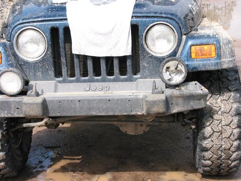 2002 Jeep Wrangler - The front grille and bumper of a blue 2002 Jeep Wrangler are visible, showing a damaged headlight and the Jeep logo.