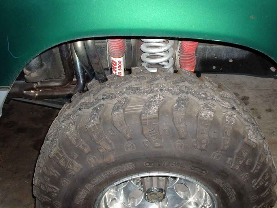 Super Swamper tire on alloy wheel under green fender with coil spring and red Rancho RS 5000 shock