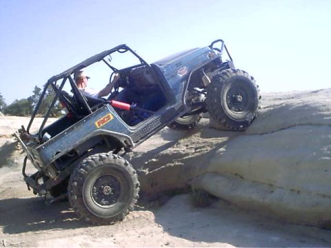 1978 Ford Bronco - A driver navigates an off-road vehicle up a steep, rocky incline under a clear sky.