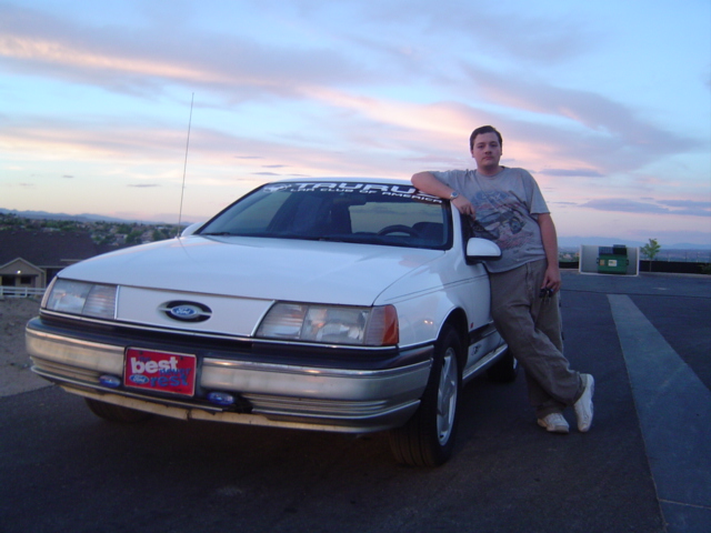 White Ford Taurus sedan at dusk with young man leaning on it