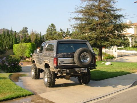 1985 Ford Bronco - Rear view of a lifted 1985 Ford Bronco with large off-road tires and a spare tire on the tailgate.