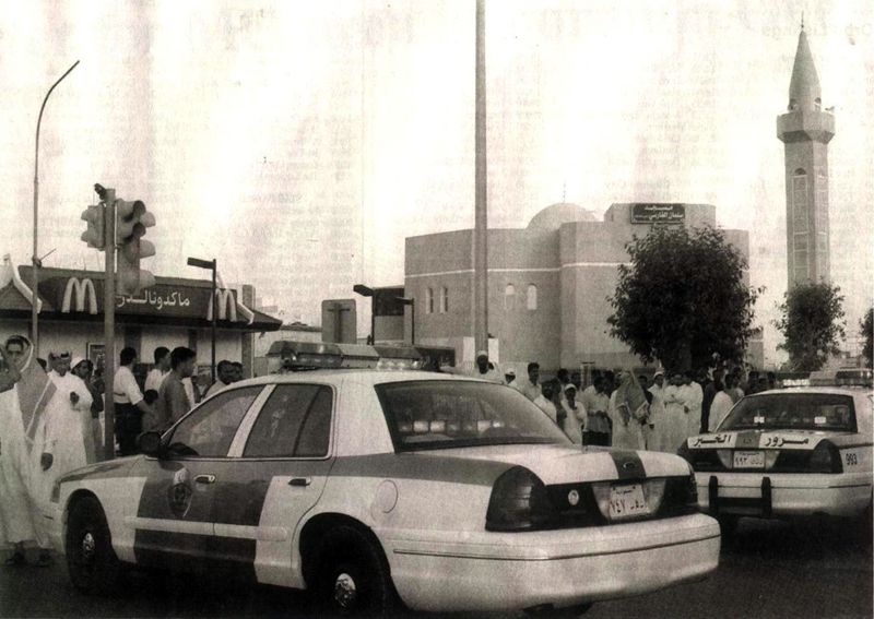 Two police cars parked outside a McDonald's with a mosque in the background. The car in the foreground has a light bar on its roof