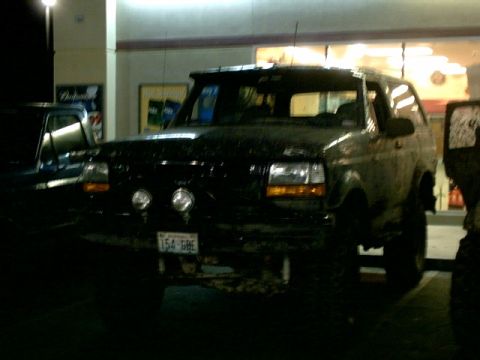 1995 Ford Bronco - A dark-colored Ford Bronco is parked at a gas station, with another vehicle visible to its left.