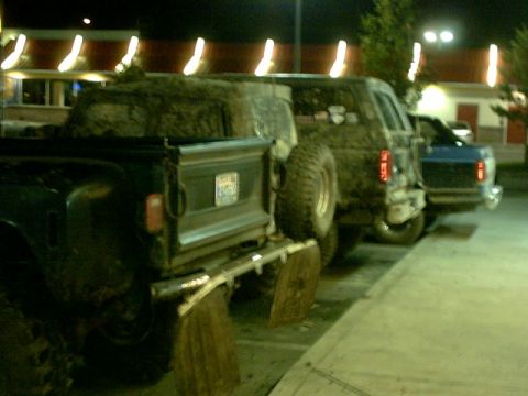 1995 Ford Bronco - Two mud-covered SUVs are parked next to each other at night, with a spare tire visible on the rear of the first vehicle.