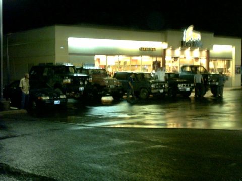 1995 Ford Bronco - Multiple vehicles are parked in a lot at night, with reflections visible on the wet ground.