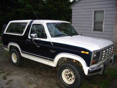 1984 Ford Bronco - Two-tone blue and white 1984 Ford Bronco parked outside a house.
