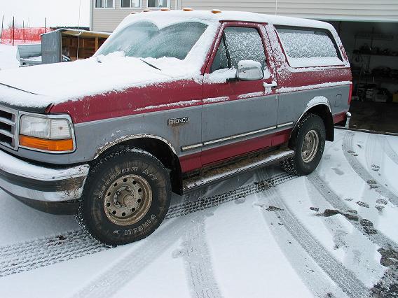 Snow-dusted red and gray Ford Bronco beside a building