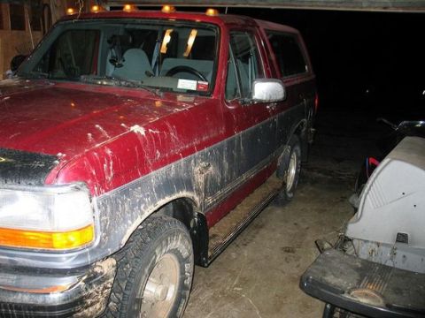 1995 Ford Bronco - This red SUV, likely a 1995 Ford Bronco, is covered in mud and parked indoors.