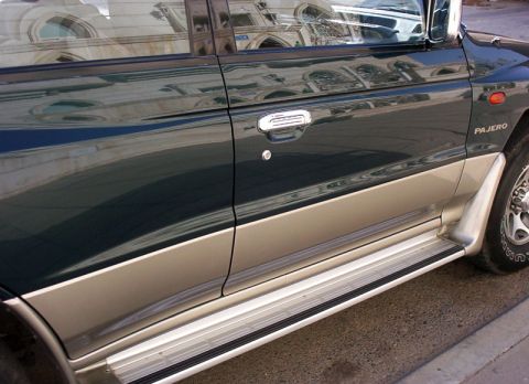 2000 Mitsubishi Montero - Side view of a dark green and tan 2000 Mitsubishi Montero, showing its running boards and door handle.