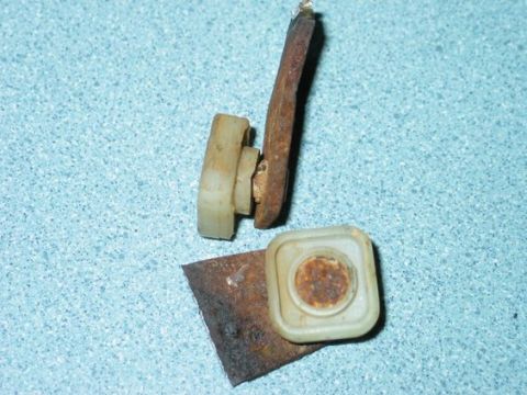 1995 Ford Bronco - Close-up of a rusty metal bracket with two plastic clips, likely a car part.