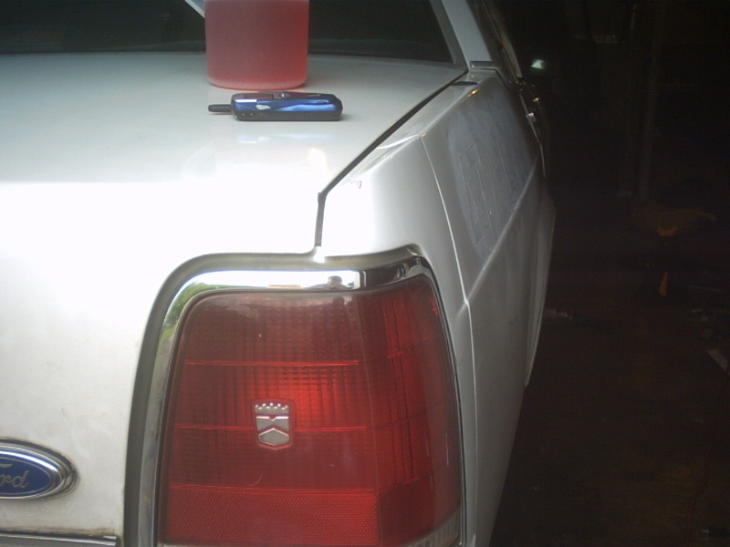 Rear corner of a white Ford sedan showing the chrome-trimmed red tail lamp and Ford oval badge