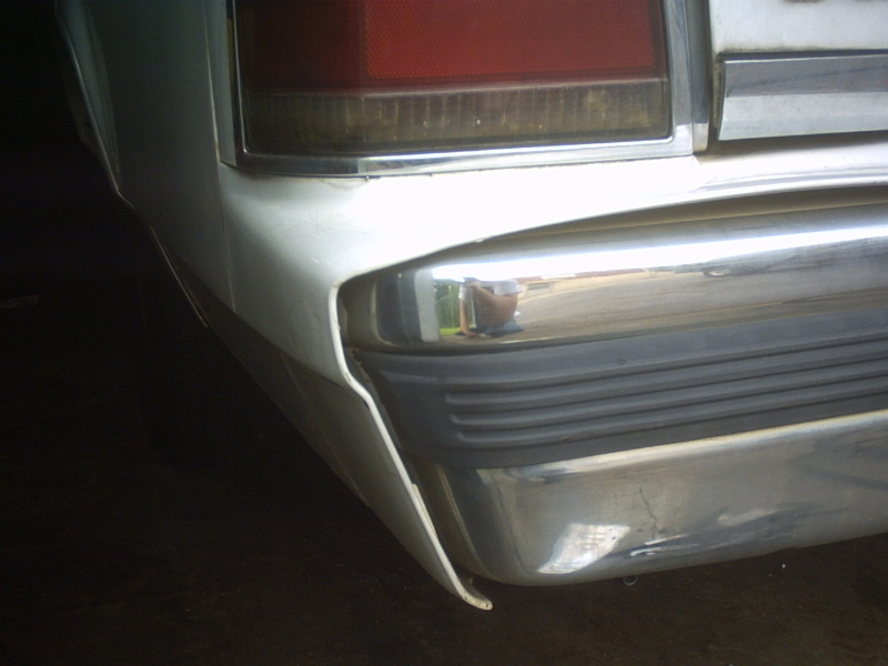 Rear corner of a white car showing a chrome bumper with black rubber trim and a red taillight